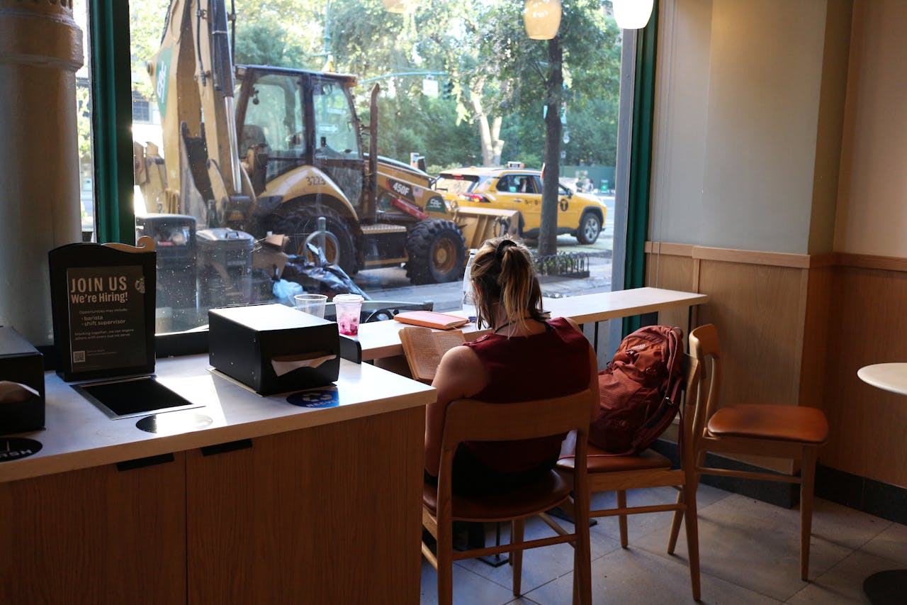 About A woman reads by the window in a coffee shop, overlooking street construction.
